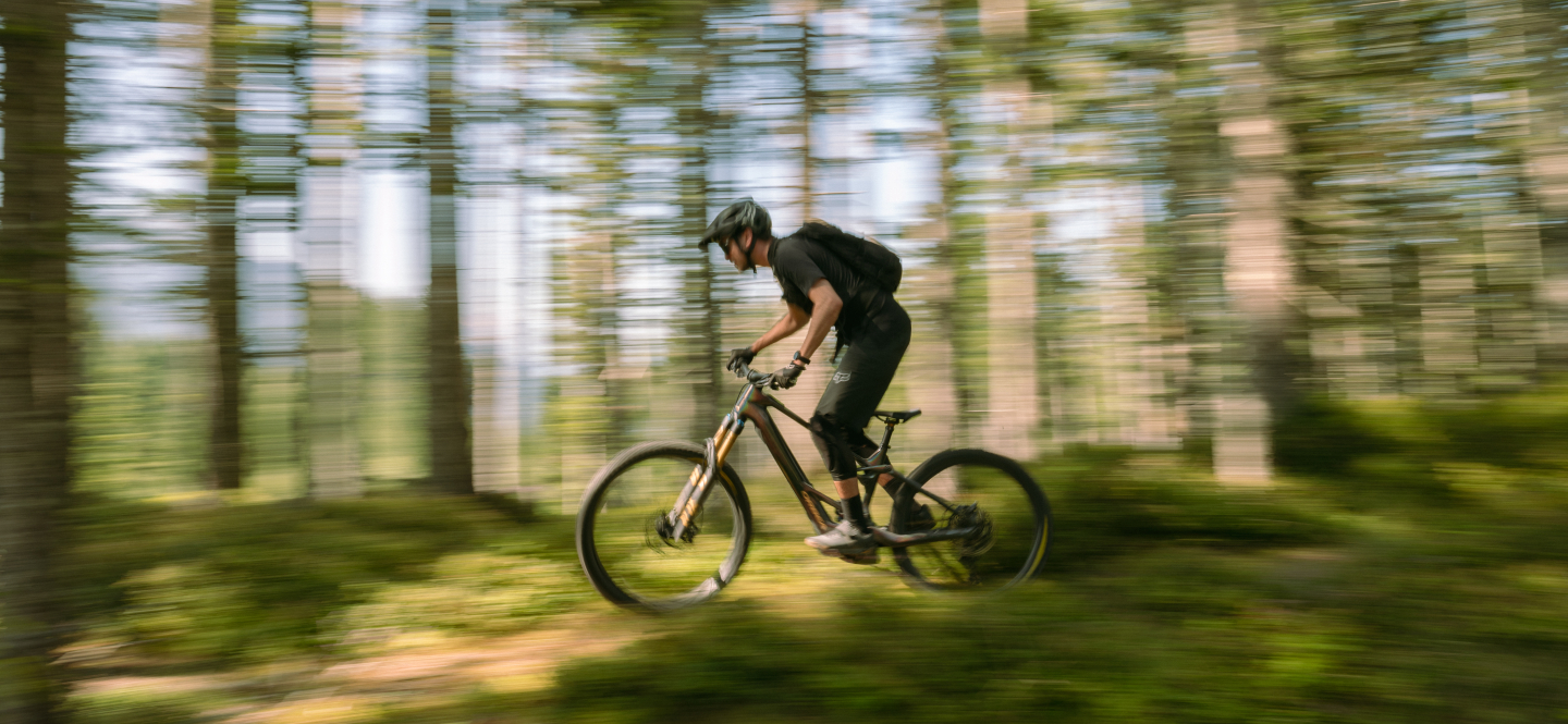 Mountainbiker fährt schnell über einen grünen Waldweg; Outdoor-Abenteuersportarten.