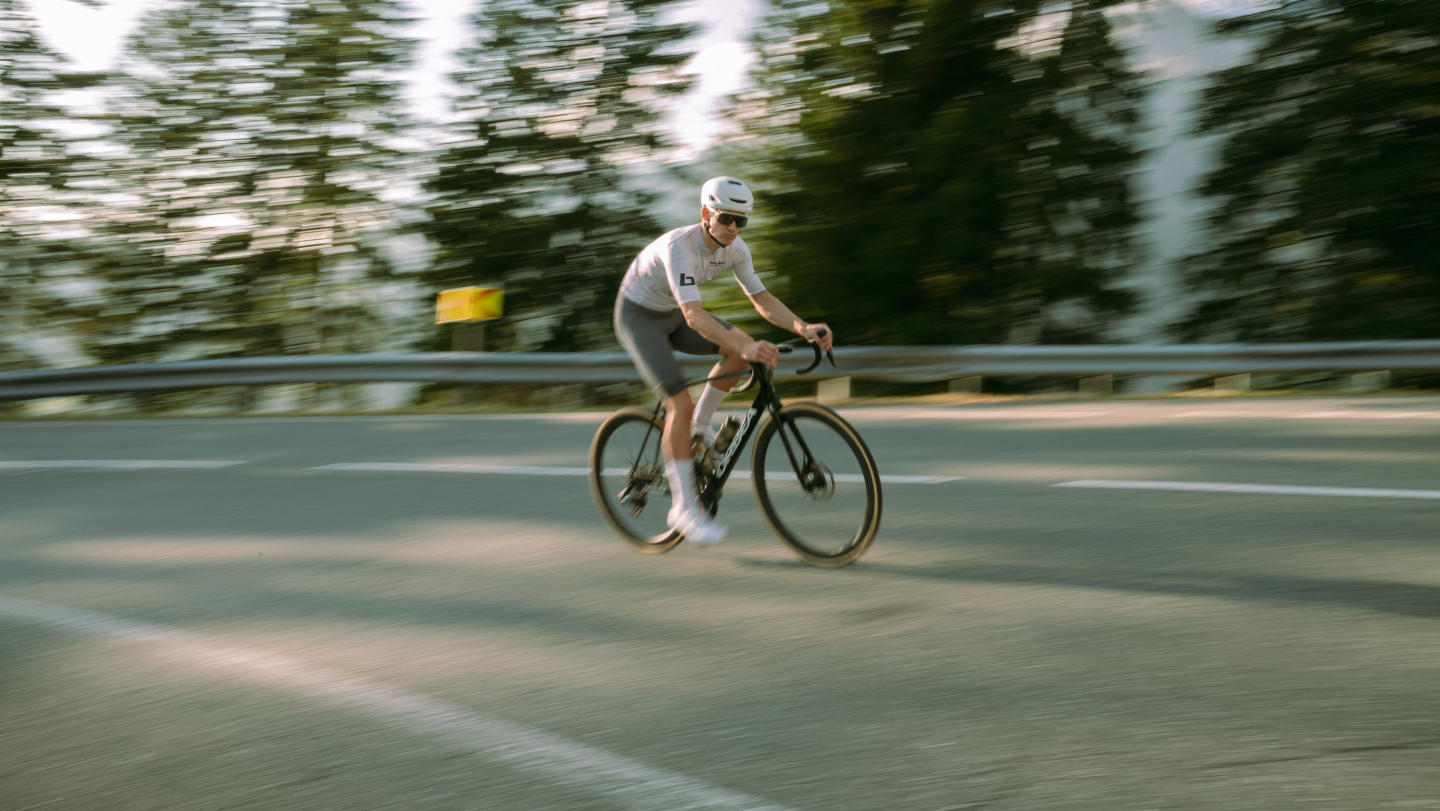 Radfahrer fährt mit einem Rennrad auf einer Bergstraße mit Bewegungsunschärfe und immergrünen Bäumen.