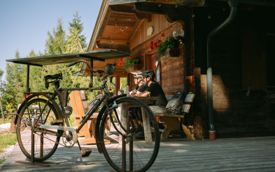Paar entspannt sich auf Bank in der Nähe einer Berghütte mit Vintage-Fahrrad; Outdoor-Reiseabenteuer.