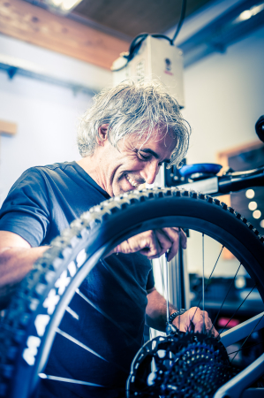 Lächelnder Mann repariert Mountainbike-Rad in der Werkstatt; Fahrradwartung und -service.