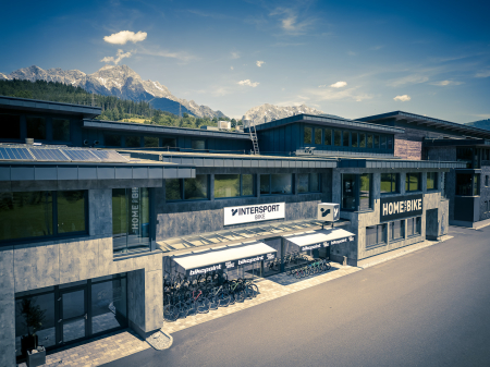 Wintersport-Skigeschäft mit Bergkulisse, Homebase-Fahrradladen und sonnig blauem Himmel.