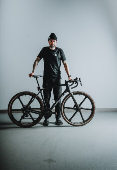 Radfahrer in Schwarz mit Gravelbike mit Carbonlaufrädern für Abenteuer-Radsport.