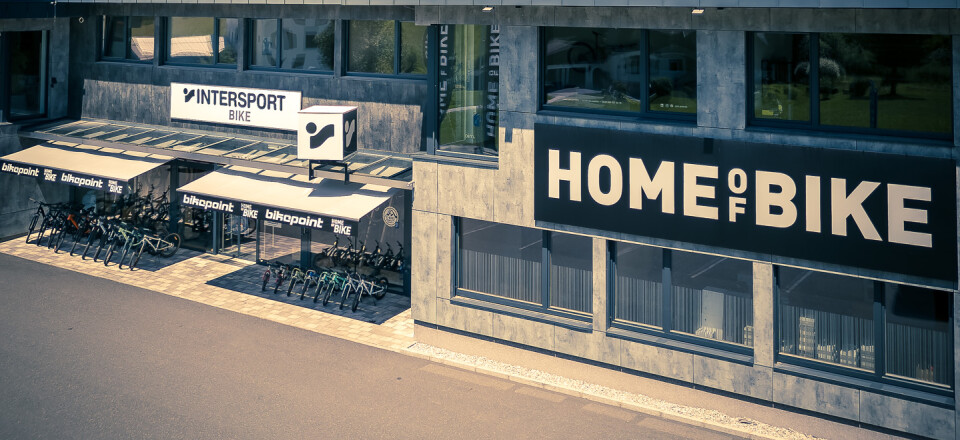 Intersport Home of Bike Store Außenansicht mit Bergkulisse, Fahrradgeschäft in Österreich.