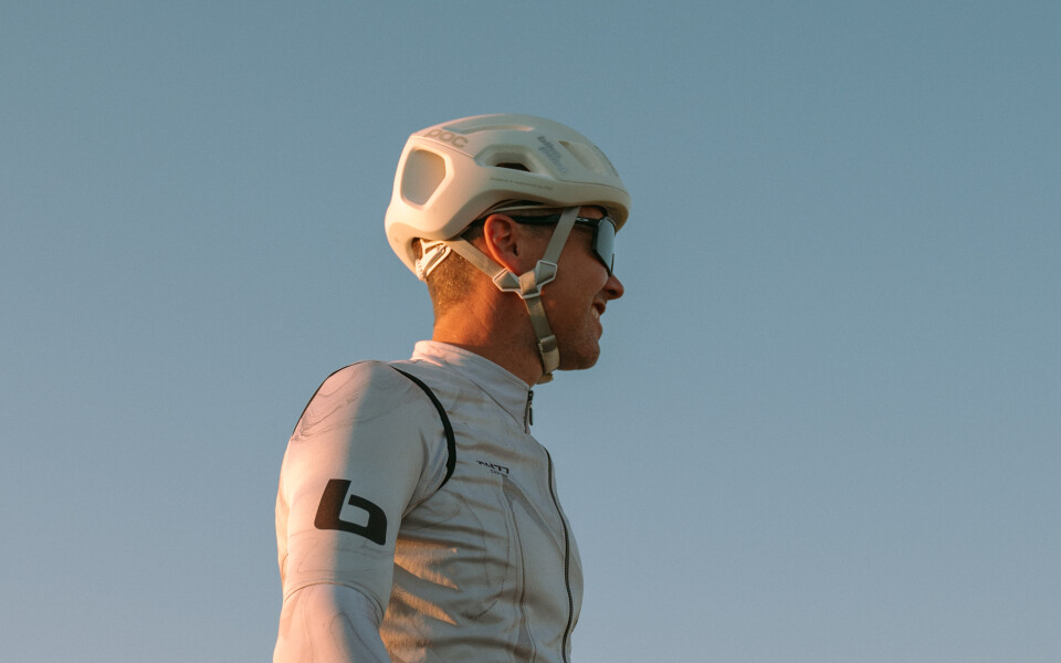 Radfahrer mit Helm und Radsportbekleidung mit Mountainbike vor klarem Himmel.