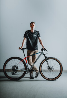 Ein Mann posiert mit einem modernen Hardtail-Mountainbike mit Reifen mit hellbrauner Seitenwand und einem grauen Rahmen.