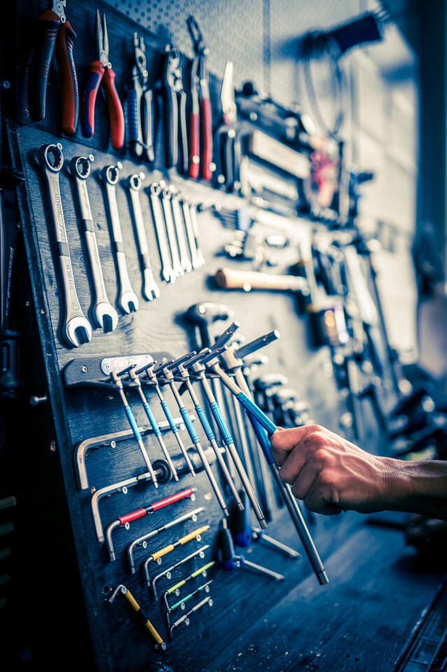 Die Hand eines Mechanikers wählt Werkzeuge von einer Werkstatt-Lochwand aus; Schraubenschlüssel, Zangen und Schraubendreher.