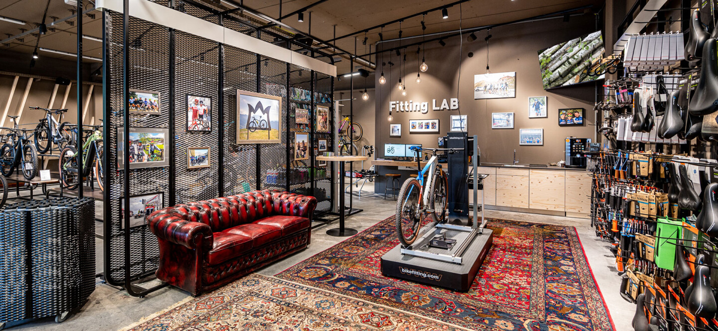 Fahrradladen-Interieur mit rotem Ledersofa, Perserteppich und Fahrradanpassungsstation.