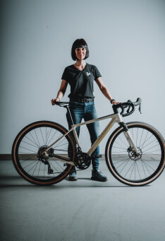 Frau posiert mit Gravelbike. Radfahrer steht neben Fahrrad mit beigen Reifen und Rennlenker.