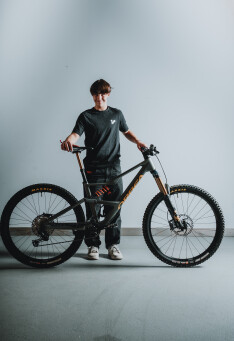 Junger Mann posiert mit einem schwarzen Mountainbike und präsentiert dessen Federung und Reifendetails.