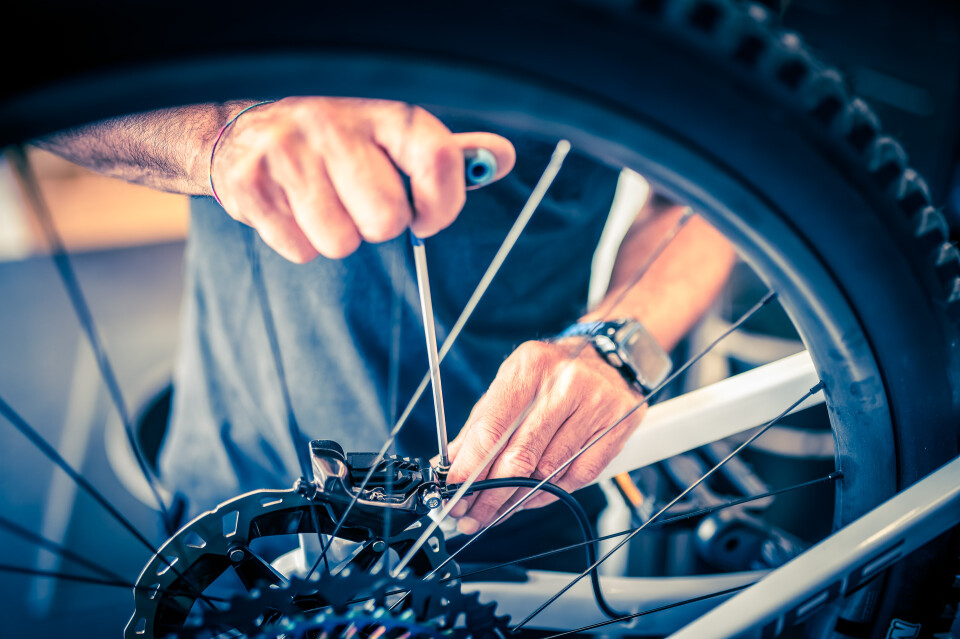 Nahaufnahme von Händen, die Fahrradspeichen mit Werkzeug reparieren. Fahrradwartung und -reparaturdienst.