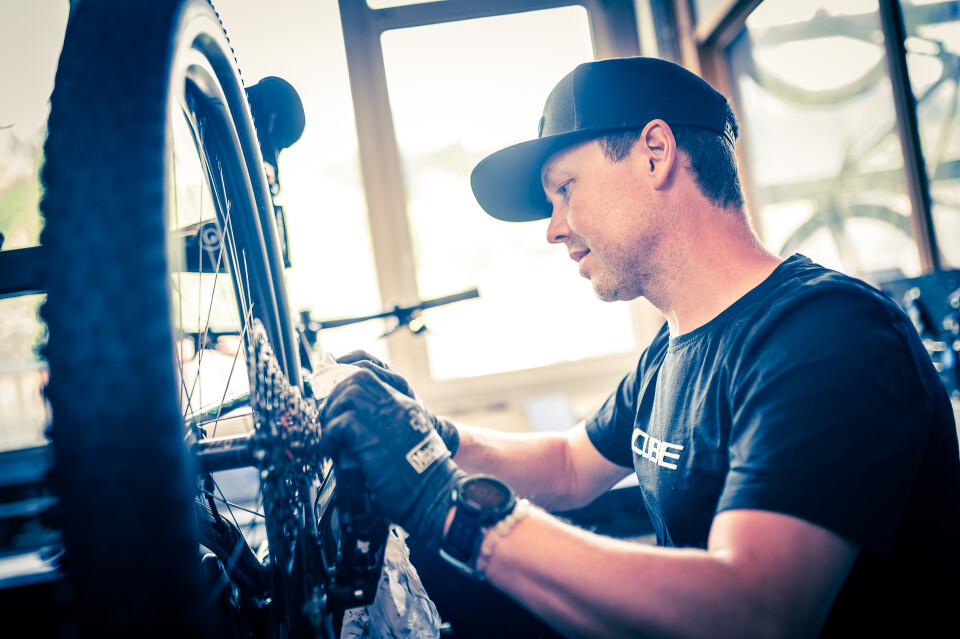 Ein Fahrradmechaniker repariert in einer Werkstatt ein Cube-Mountainbike, wobei der Fokus auf dem Schaltwerk liegt.
