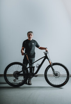 Mann posiert mit schwarzem vollgefederten Mountainbike in einer Studio-Umgebung für ein Fahrrad-Lifestyle-Shooting.