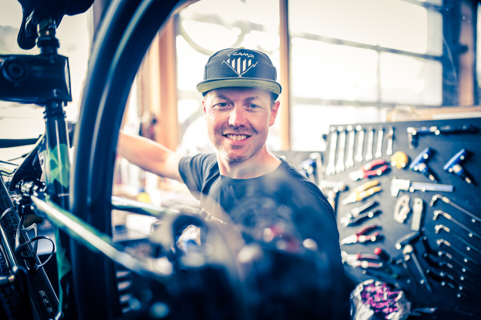 Lächelnder Fahrradmechaniker in der Werkstatt mit Werkzeugen, der ein Fahrradrad für den Fahrradservice repariert.